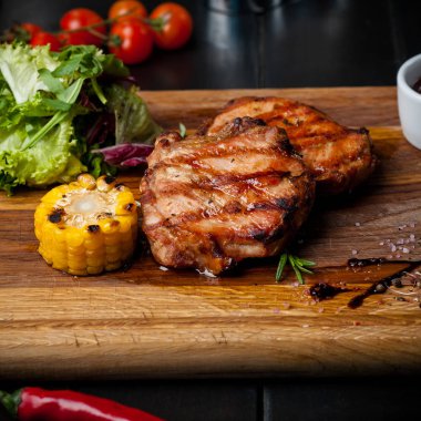 Mısır ve salata bir ahşap tahta üzerinde iki ızgara biftek.