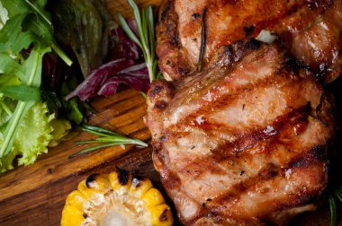 Mısır ve salata bir ahşap tahta üzerinde iki ızgara biftek.