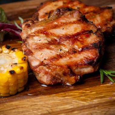 Mısır ve salata bir ahşap tahta üzerinde iki ızgara biftek.