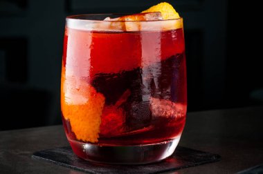 Barmen turuncu ve buz bir kokteyl yapar. Makro, siyah arka plan, el, kırmızı