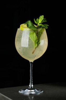 Limon ve nane bir bardak buz içinde sarı serinletici içecek. Bubbles ve çiğ siyah bir zemin üzerine kokteyl