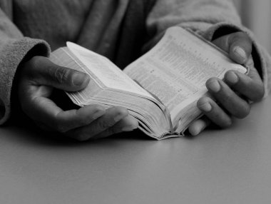 Adam gri arka planda elleri İncil 'in üzerinde dua ediyor.