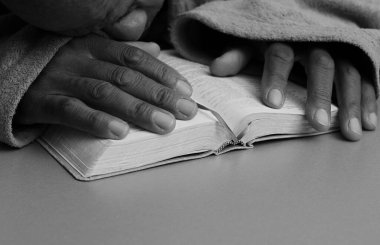 Adam gri arka planda elleri İncil 'in üzerinde dua ediyor.