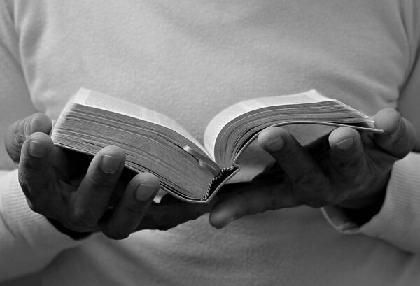 Man praying with hands on bible on grey background