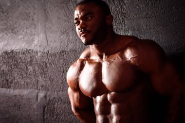 Vücut geliştirici duvara yaslanmış duruyor. Afrikalı Amerikalı erkek sporcu kas gelişimini gösteriyor