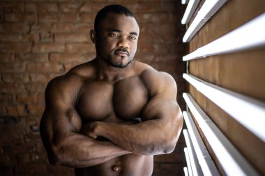 Güçlü Afroamerikan atletik adam mükemmel şekilli kaslı tuğla arka planda gün ışığı lambalarının yanında