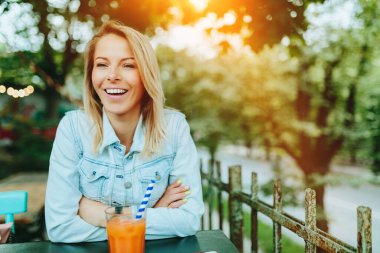 Kaldırımdaki kafede elinde bir bardak havuç suyu olan genç bir kadın. Yumuşak odaklanma, iyi film kazanım dokusu.