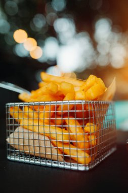 Kafe masasında bir sepet kızarmış patates. Yumuşak odaklanma, iyi film kazanım dokusu.