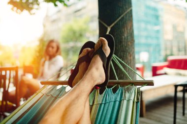 Hamakta dinleniyor. Parmak arası terlikli erkek ayakları. Yumuşak odaklanma, iyi film kazanım dokusu.