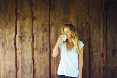 Tahta duvarın önünde sabah kahvesini içen genç bir kadının portresi.