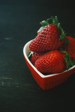 Siyah ahşap arka planda küçük bir kasede lezzetli kırmızı çileklerin yakın plan çekimi.