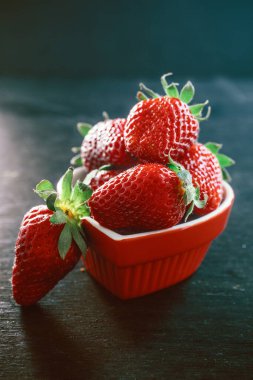 Siyah ahşap arka planda küçük bir kasede lezzetli kırmızı çileklerin yakın plan çekimi.