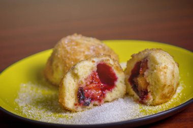 Şeker ile taze erik köfte. Bir dilimlenmiş dumpling ve koyu kırmızı masada sarı plaka üzerinde bir delik.