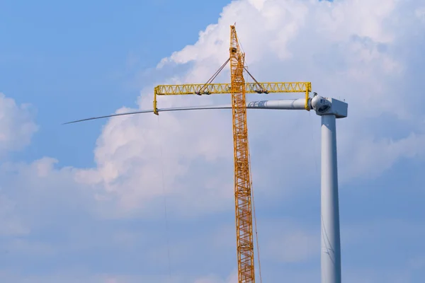 yellow crane tower placing windmill blade with background of blue sky.