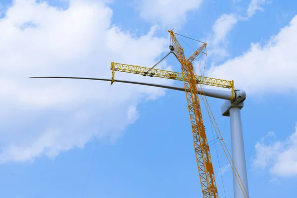 yellow crane tower placing windmill blade with background of blue sky. Wind Turbine Construction.