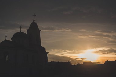 Arka planda bulutlu gökyüzü ve güneş ile günbatımı Ortodoks kilise silüeti.