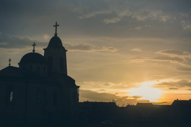 Arka planda bulutlu gökyüzü ve güneş ile günbatımı Ortodoks kilise silüeti.