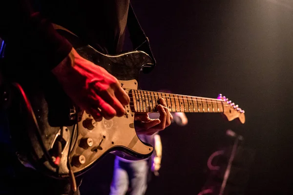 O guitarrista toca uma guitarra elétrica no palco com luzes no fundo. Fechar — Fotografia de Stock