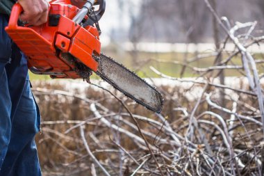 Mavi pantolonlu yaşlı adam tutun turuncu chainsaw kendi elleriyle.
