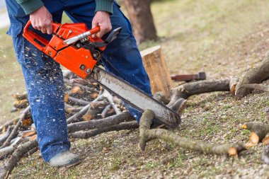 Turuncu testere çıplak elleri ile tutarak ve yere yerleştirilen bir dal kesme ihtiyar. Eylem turuncu chainsaw.