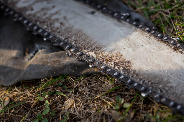 Закрыть грязную цепь бензопилы, расположенную на земле на траве
.