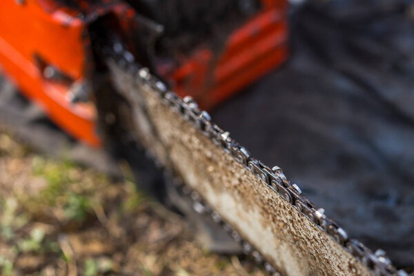 Закрыть грязную цепь бензопилы, расположенную на земле на траве
.