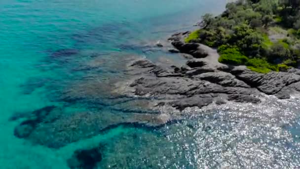 光の反射と岩の海岸の青い海面の航空写真 透明なターコイズブルーの海水面と海岸の岩のトップビュー — ストック動画