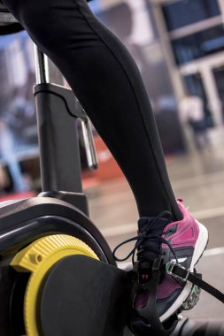 Eğitim için spor salonunda siyah ve sarı spor bisiklet kız ayak yakın.