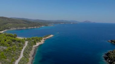 Ağaçlarla çevrili mavi deniz yüzeyinin havadan drone görünümü. Koyu mavi okyanus su yüzeyi, deniz kıyısı, orman, araba yolu üst görünümü.