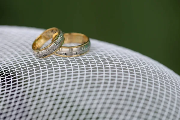 Anéis de casamento dourados na malha branca com fundo verde — Fotografia de Stock