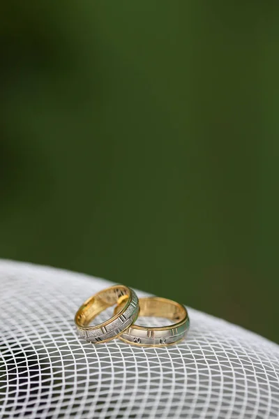 Anéis de casamento dourados na malha branca com fundo verde — Fotografia de Stock