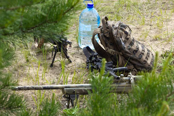 Drei Gewehre, Rucksack und Wasserflasche auf dem Boden im Wald, Armeewaffe des aktiven militärischen Spiels Airsoft — Stockfoto