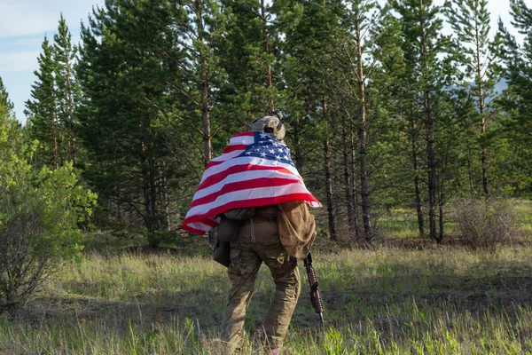 미국 국기를 든 완전 무장한 미국 군인은 여름 숲에서 실행됩니다. 활발히 진행되는 군사 게임 에어 소프트. — 스톡 사진