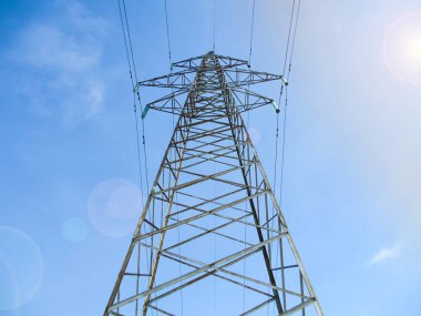 Mavi gökyüzü ve güneş parlayan yüksek voltajlı kulelerde elektrik iletim hatları.
