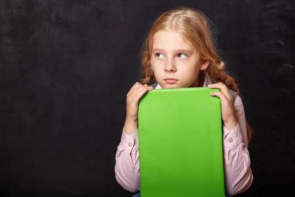 Scolaretta con un libro su sfondo lavagna — Foto Stock