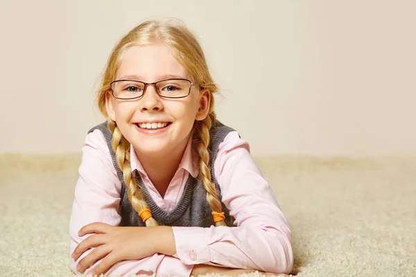 Mädchen im Schulalter mit Brille auf einem Teppich — Stockfoto