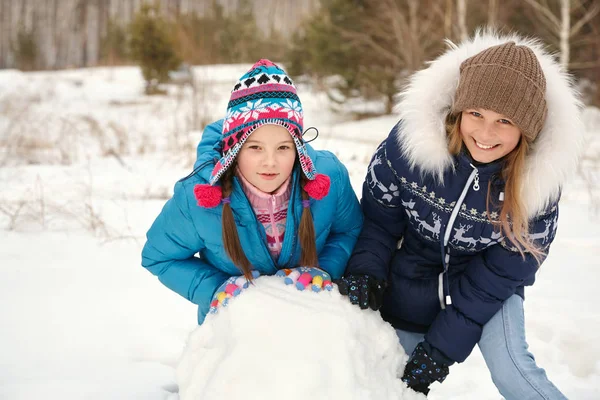 Две девушки зимой строят снеговика. — стоковое фото
