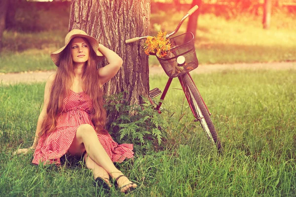 Jovem mulher em um chapéu com bicicleta em um parque — Fotografia de Stock