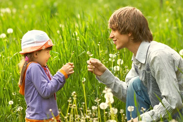 Far och dotter leker i gräset med maskrosor — Stockfoto