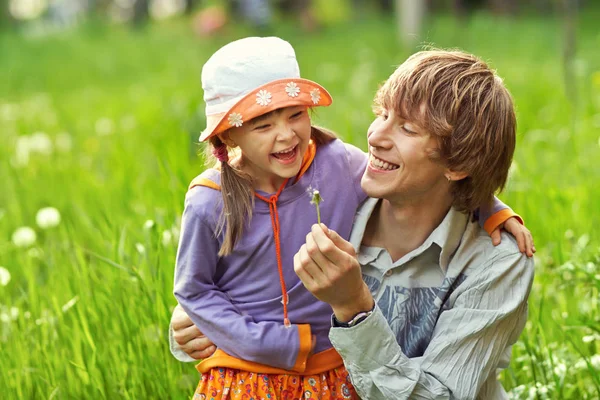 Far och dotter leker i gräset med maskrosor — Stockfoto