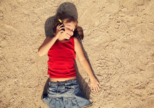 Liten jente i sanden med mobiltelefon – stockfoto