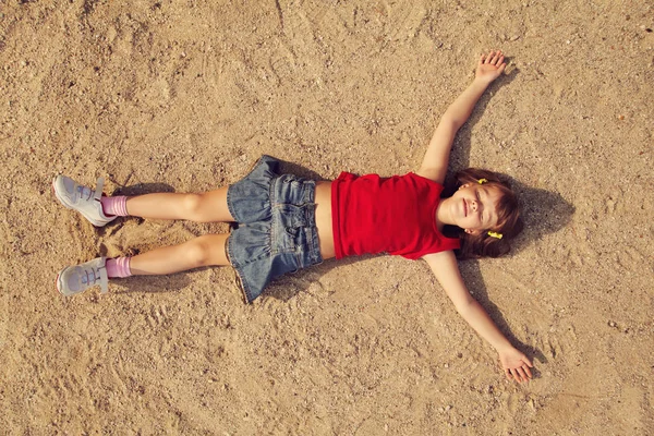 Χαμογελώντας χαλαρώνετε ξαπλωμένοι στην αμμουδιά το χαριτωμένο μικρό κορίτσι — Φωτογραφία Αρχείου