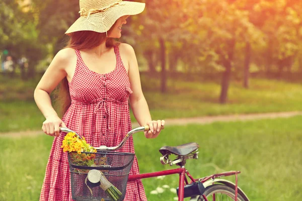 Giovane donna in abito e cappello con una bicicletta con fiori in un cesto — Foto Stock