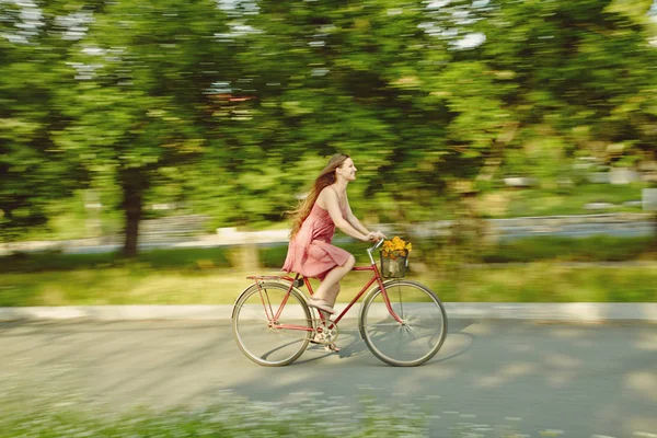 Jonge vrouw in een jurk rijdt een fiets in een zomer-park — Stockfoto