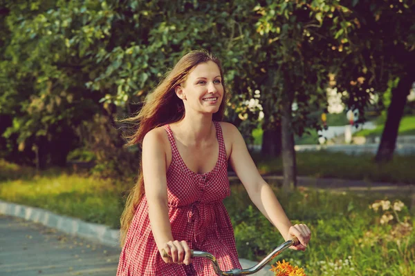 Młoda kobieta w sukni jeżdżę rowerem w lato park — Zdjęcie stockowe