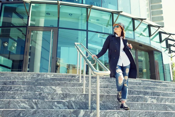 Стильная женщина в шляпе и солнцезащитных очках на ступеньках торгового центра — стоковое фото