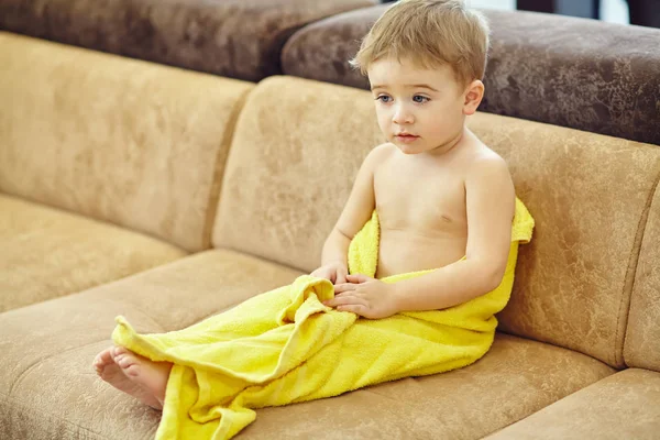 Junge in Handtuch gewickelt und nach der Dusche auf Couch getrocknet Stockbild