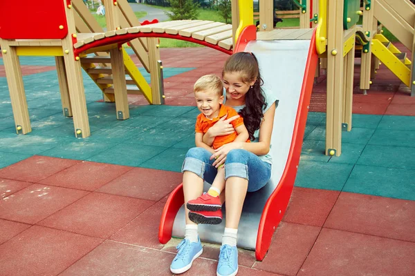 Ragazzino al parco giochi. giocare bambino con la madre su uno scivolo — Foto Stock