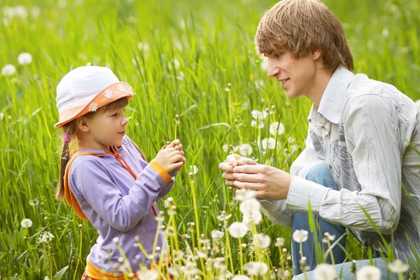 Father and daughter blowing on dandelions in a summer — Stock Photo, Image