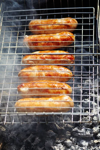 Salchichas rubicundas asadas sobre carbones. Barbacoa a la parrilla en humo —  Fotos de Stock